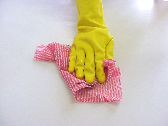 ruka ve žluté rukavici čistící bílý povrch